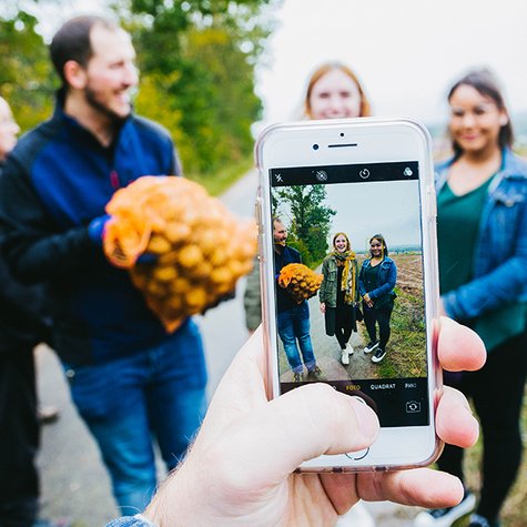Ein Tafel-Aktiver fotografiert mit seinem Smartphone andere Ehrenamtliche, die einen vollen Kartoffelsack tragen.