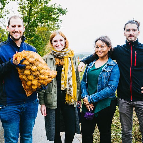 Tafel-Helferinnen und Tafel-Helfer stehen zusammen am Feld und zeigen einen Sack selbst geerntete Kartoffeln.